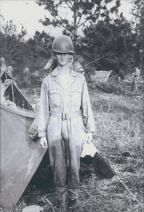 Easy Company soldier Robert Rader standing in front of a tent surrounded by fellow men.