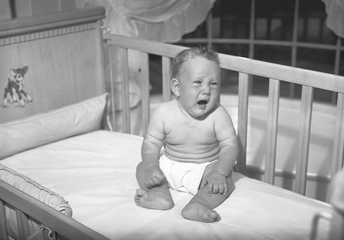 A black and white photo of a baby in a crib captures the essence of dependence.