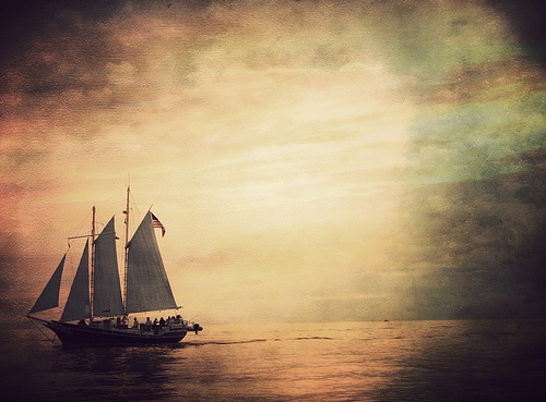 A sailboat gracefully glides across the vast ocean, capturing the beauty of a breathtaking sunset.