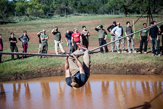 Atomic Athlete Vanguard Man hanging from Rope over Mud pit.