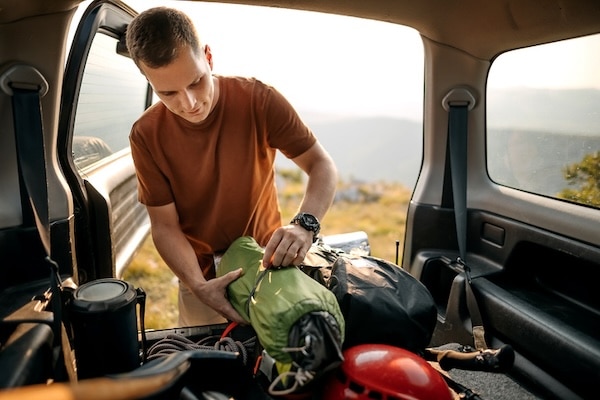 Man packing camping gear into a vehicle at dusk.