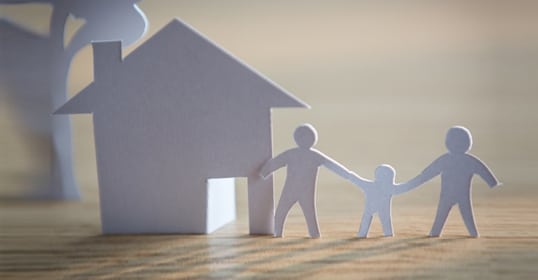 Paper cut-outs of a family with kids holding hands in front of a house silhouette.