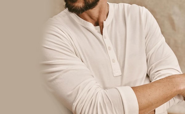 Man in a white long-sleeve Henley shirt with folded arms, showcasing one of the stylish ways to wear it.