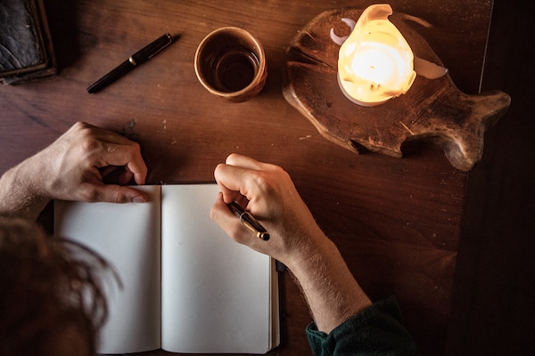 Person journaling techniques in a notebook by candlelight with a cup of coffee nearby.