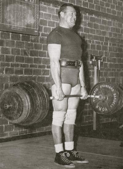 A man holding a barbell in front of a brick wall looks stronger.