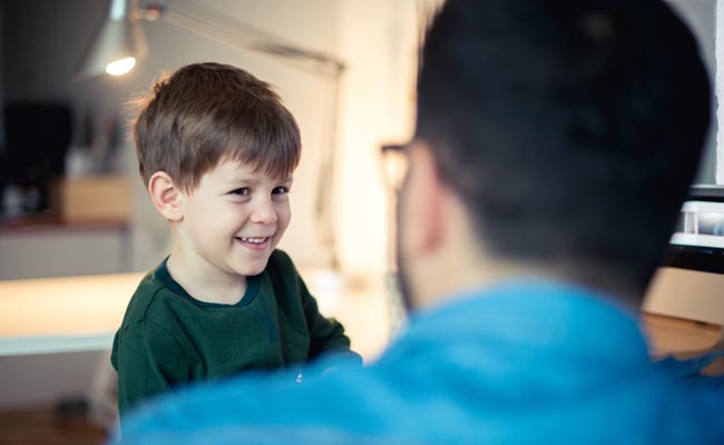 A little boy is happily smiling at a man in front of a computer.