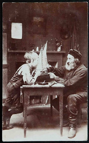 A timeless photo capturing the nostalgic bond between a man and a boy as they joyfully play with a sailboat.