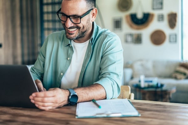 Man smiling while working on a laptop at a home office, boosting his productivity.