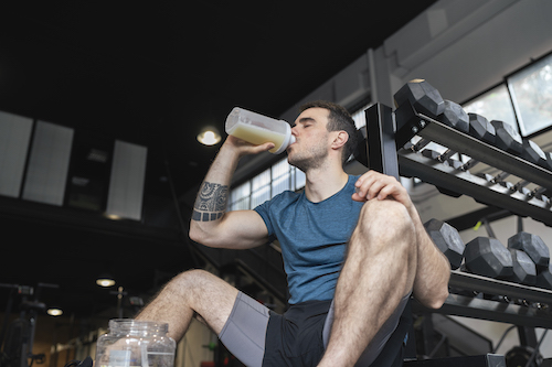 A man drinking a green protein shake in a gym.