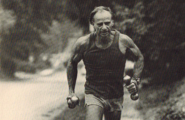 A man from the 1980s is jogging along a road with dumbbells, working on his walking workout to get in shape.