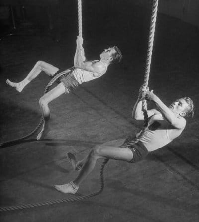 Two men engaging in guide training on thick ropes in a gym.