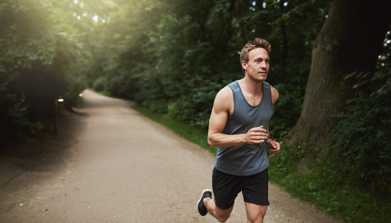 A man is jogging on a path in the woods, keeping his body parts active and relaxed.