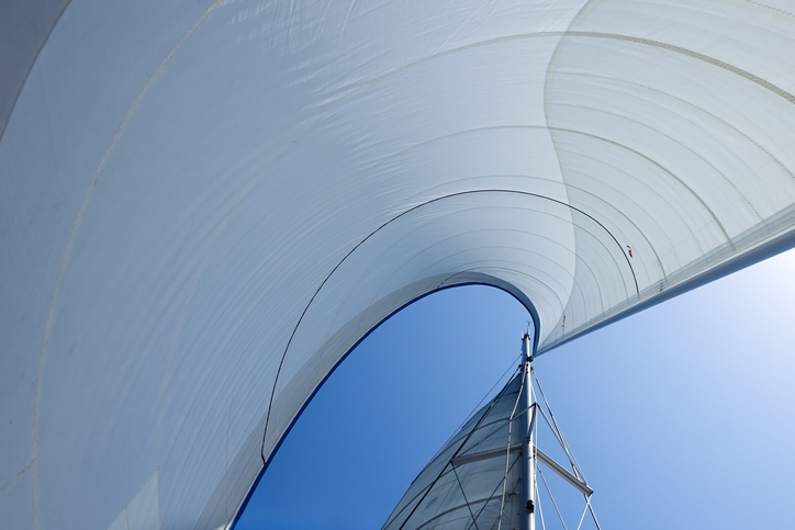 A view of a sailboat with a white sail, floating peacefully on the water.