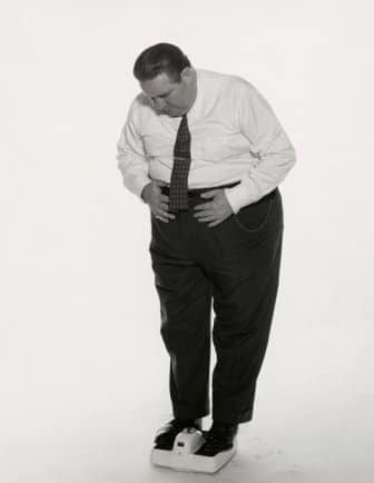 A black and white photo of a man chef standing on a scale and losing weight.