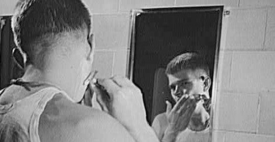 An older man is brushing his teeth in front of a mirror.