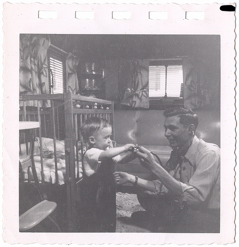 A man is teaching his son, holding him in a crib.