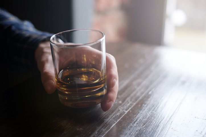 Enhance the image of a man enjoying whiskey, holding a glass on a wooden table.