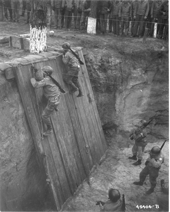 A group of soldiers, demonstrating the importance of physical fitness, are climbing over a wall during WWII Workout Week.