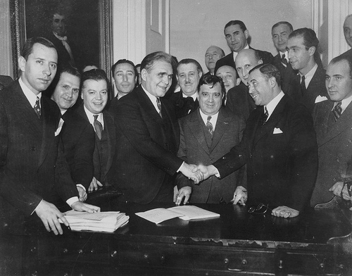 A group of men are meeting and shaking hands to strengthen their introductions at a table.