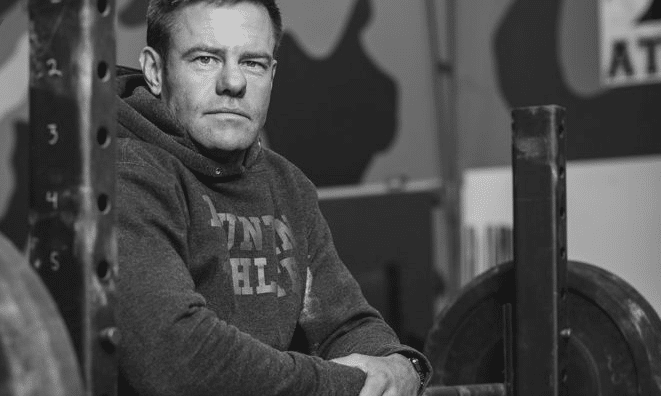 A man sitting in front of a barbell in a gym, Tactical Athlete.