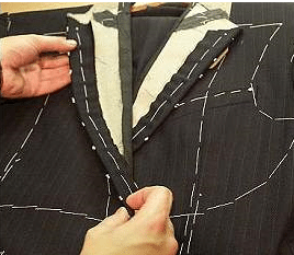 A man, skilled in the art of manliness, meticulously sews a suit on a table at Suit School.