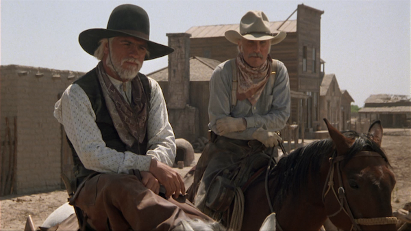 Two men in cowboy hats, one with a Podcast microphone, sitting on a horse.