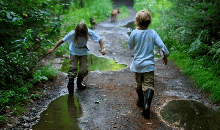 Two children running down a muddy path in the woods, establishing their connection with nature.