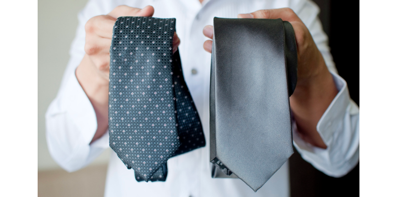 A man is holding two ties in front of a white background.