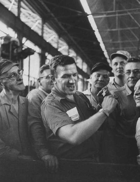 A black and white photo of a group of people in a factory, working diligently to ensure quality watch production.