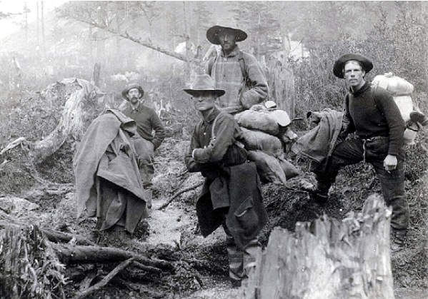 A group of men standing in the wooded area, dressed in outdoor gear.